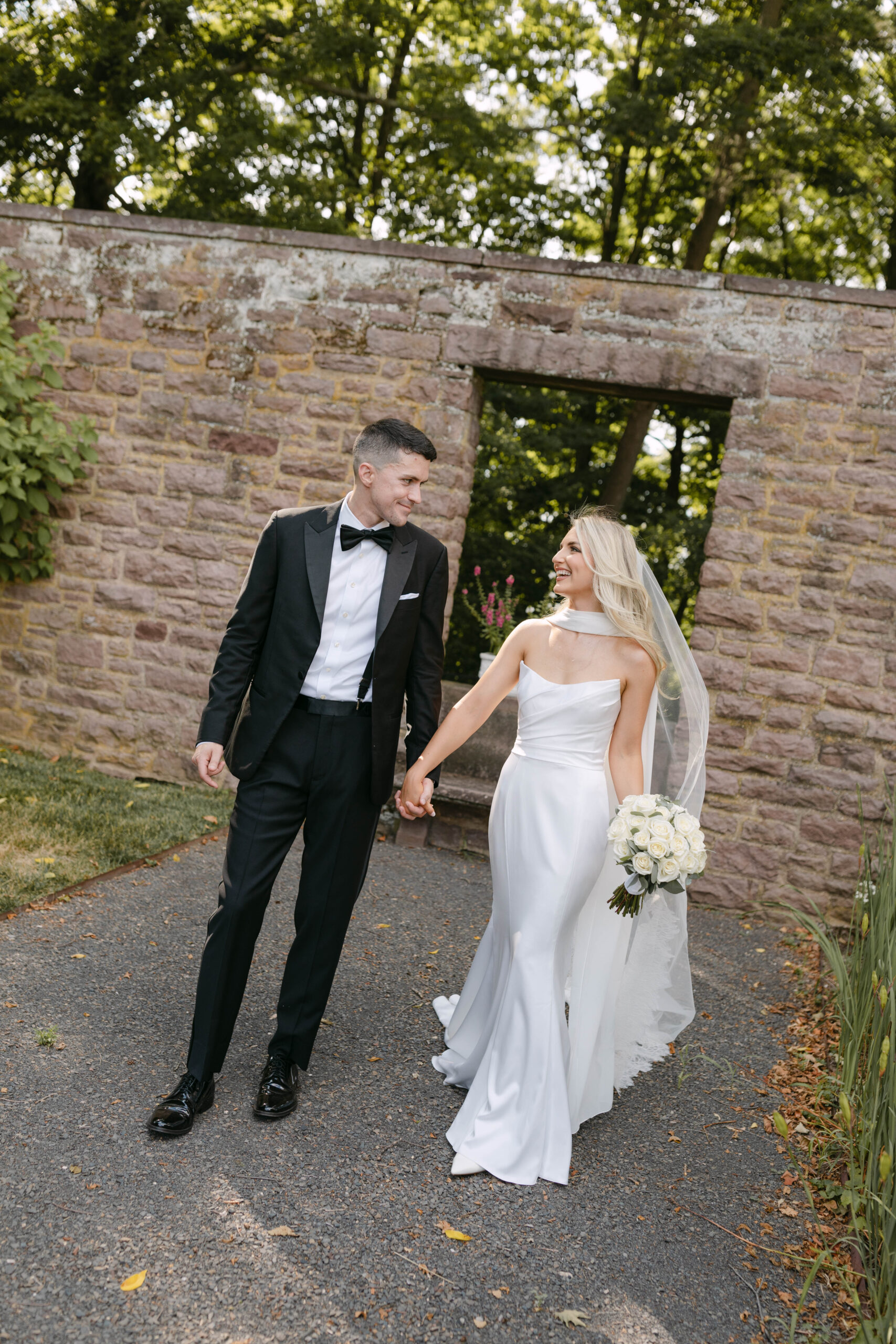 the bride and groom pose for portraits in a classic timeless white gown and black tuxedo in the lush gardens of Tyler Gardens