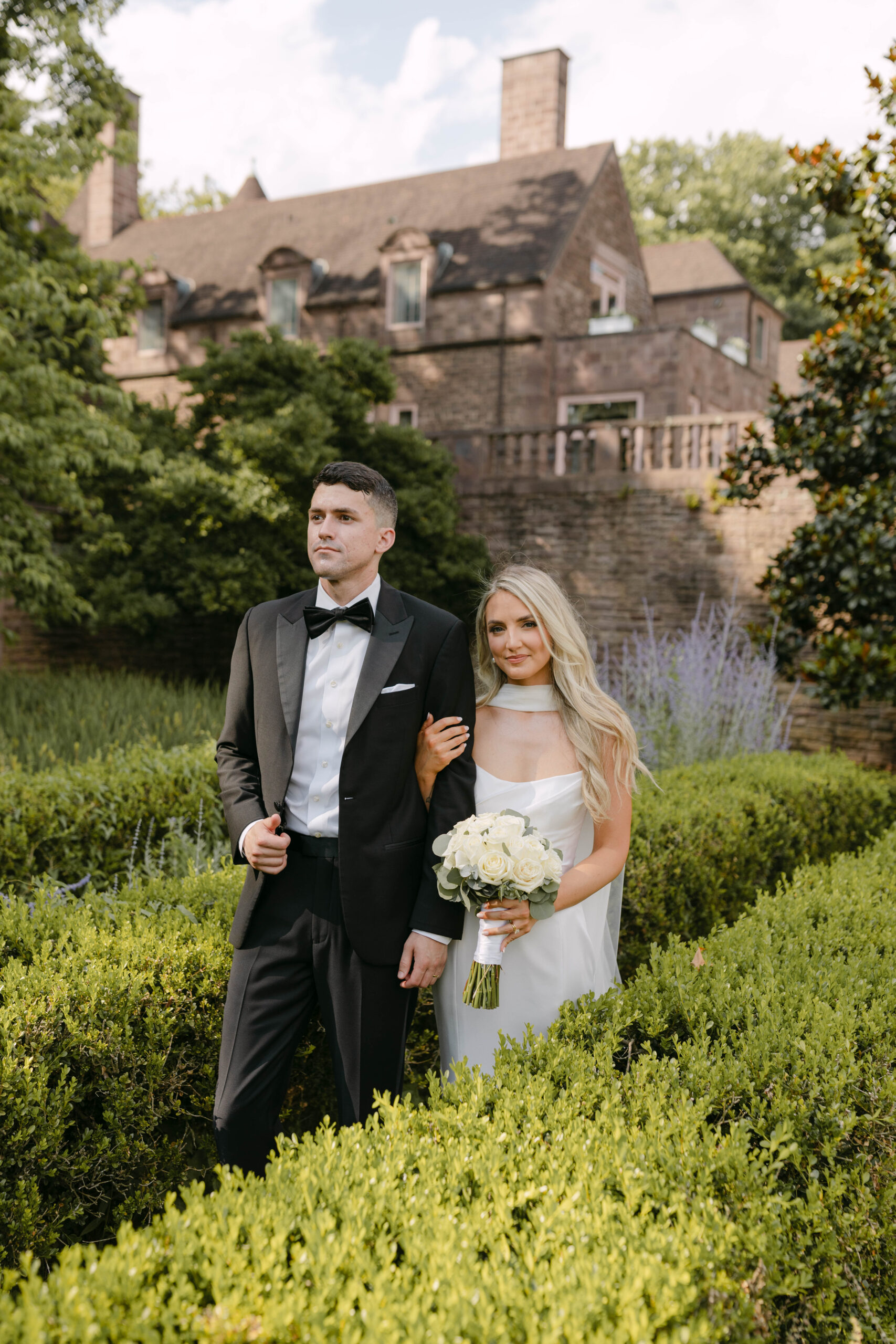 the bride and groom pose for portraits in a classic timeless white gown and black tuxedo in the lush gardens of Tyler Gardens