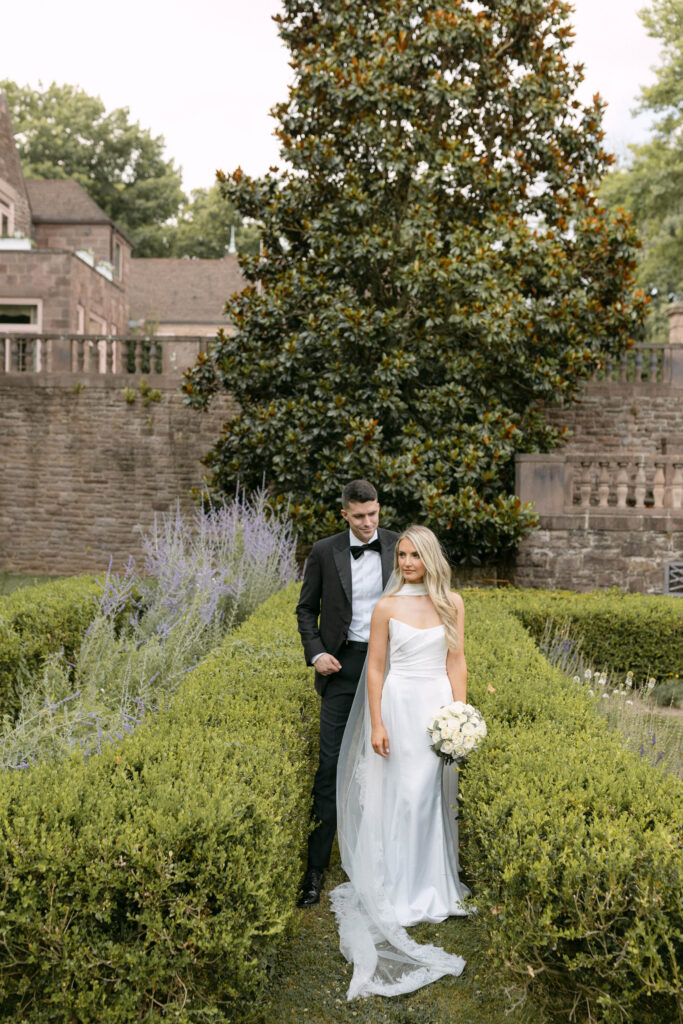 the bride and groom pose for portraits in a classic timeless white gown and black tuxedo in the lush gardens of Tyler Gardens