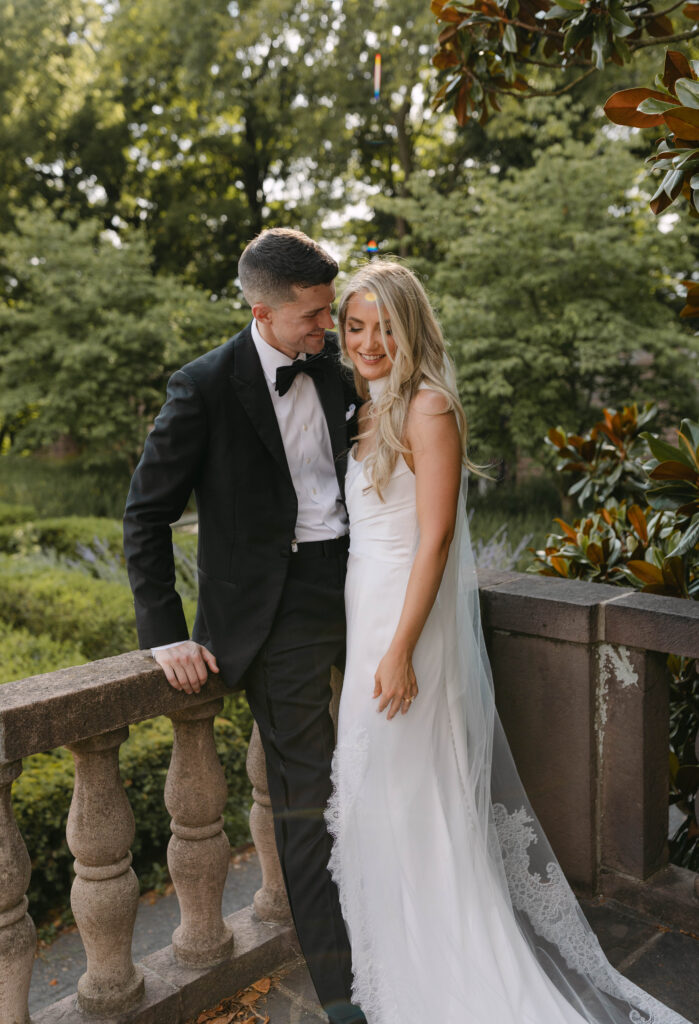 the bride and groom pose for portraits in a classic timeless white gown and black tuxedo in the lush gardens of Tyler Gardens