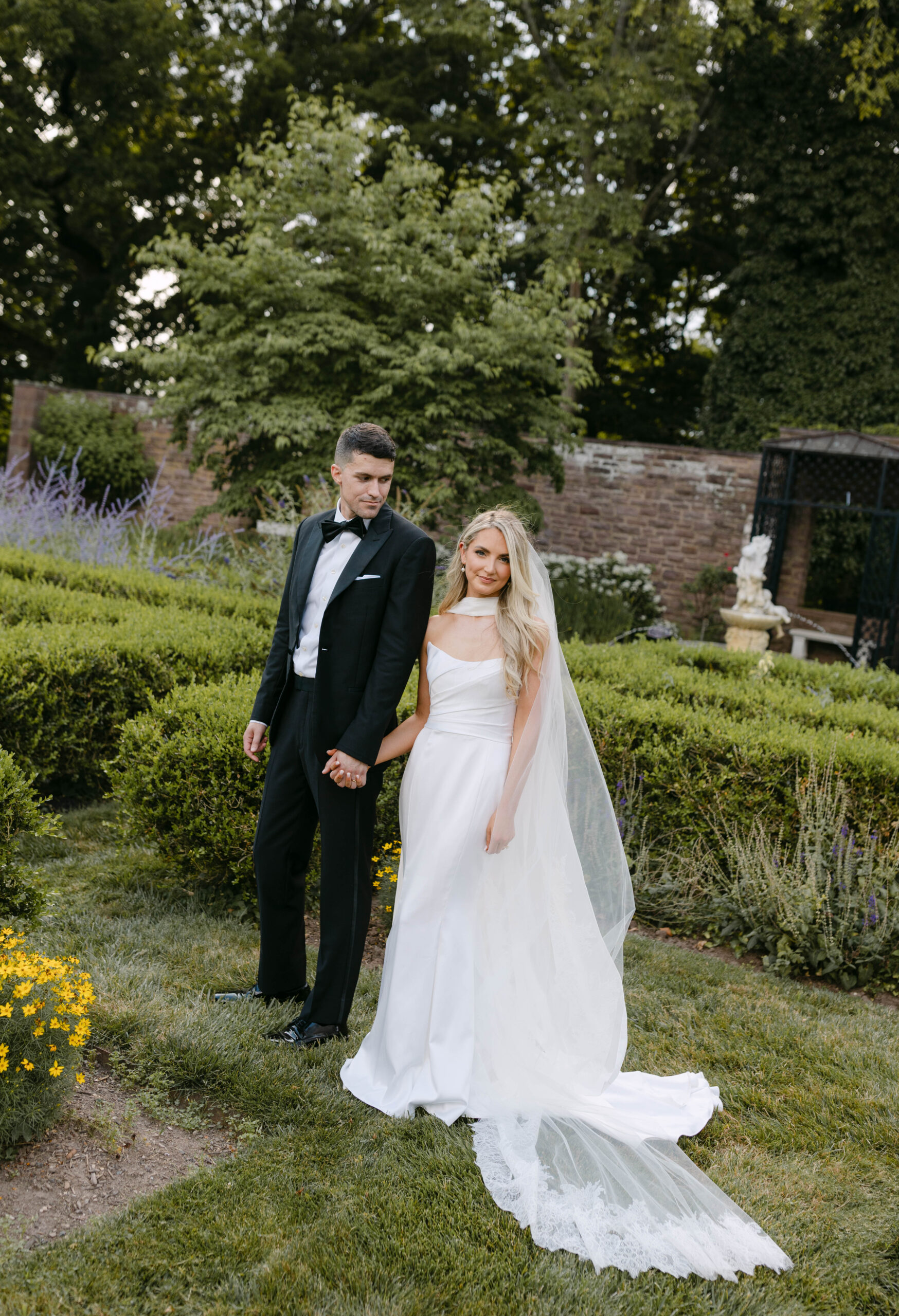 the bride and groom pose for portraits in a classic timeless white gown and black tuxedo in the lush gardens of Tyler Gardens